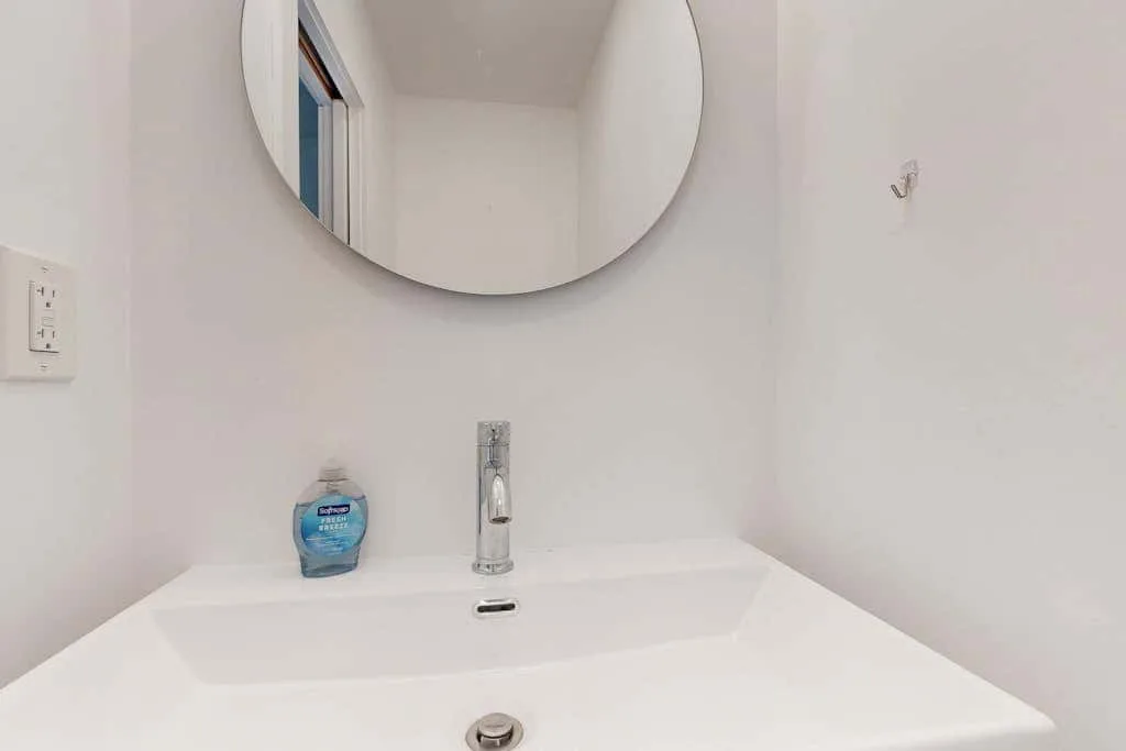 A bathroom sink and faucet sit below a round wall mirror.