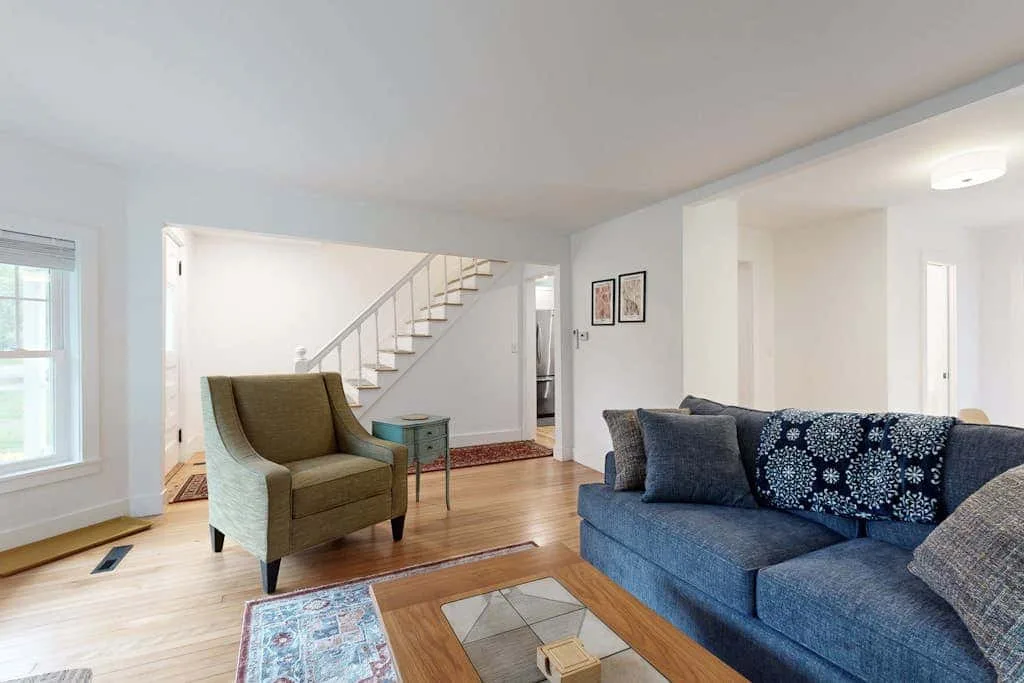 A bright living room with blue seating and a staircase in the background.