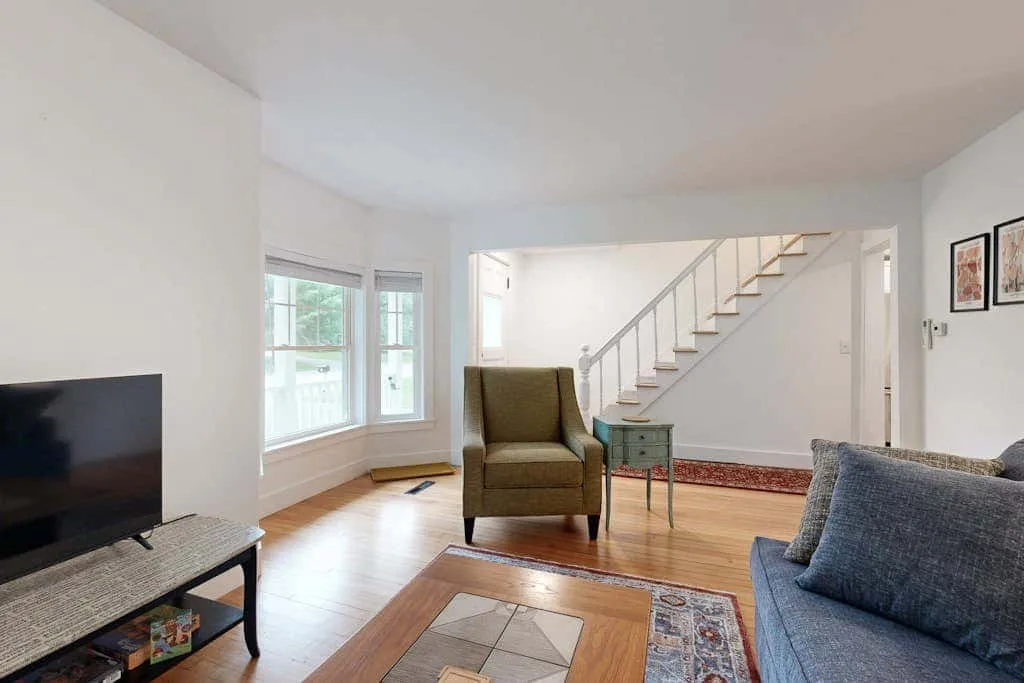 A bright living room with seating, a television, and a staircase.