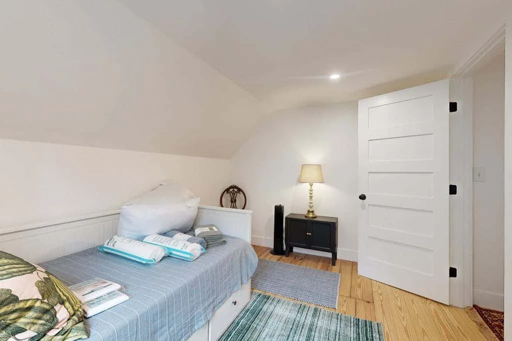 A bedroom with a bed, bedside table, and an open white door.