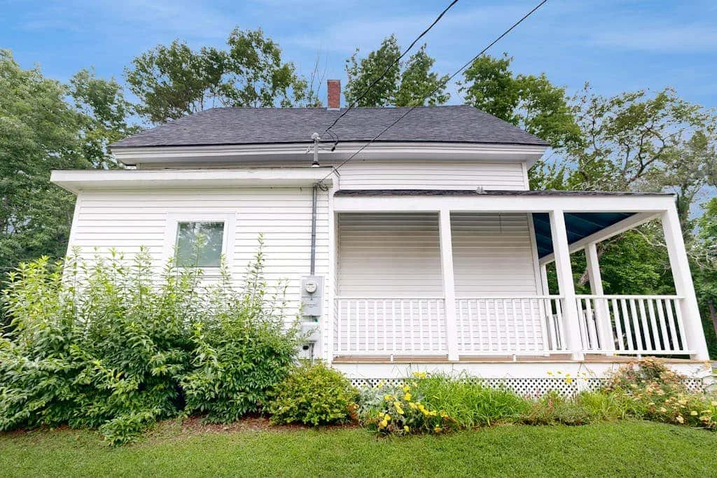 A white house with a covered porch and green shrubs in front.
