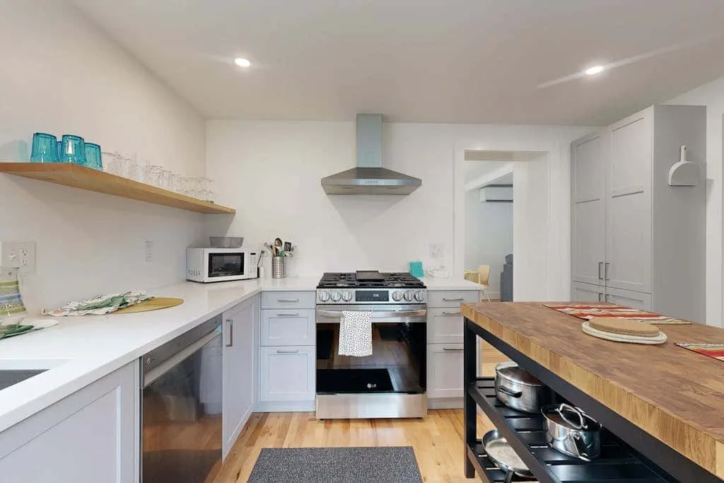 A bright kitchen with white cabinetry, a stove, and a central wood-topped island.