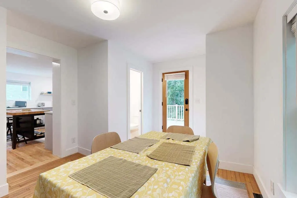 A dining area with a rectangular table set with placemats beside an open kitchen.