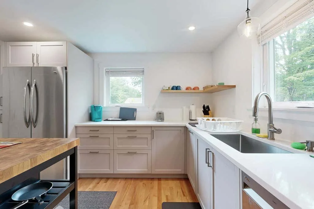 A bright kitchen with white cabinetry, stainless steel appliances, and a central worktable.