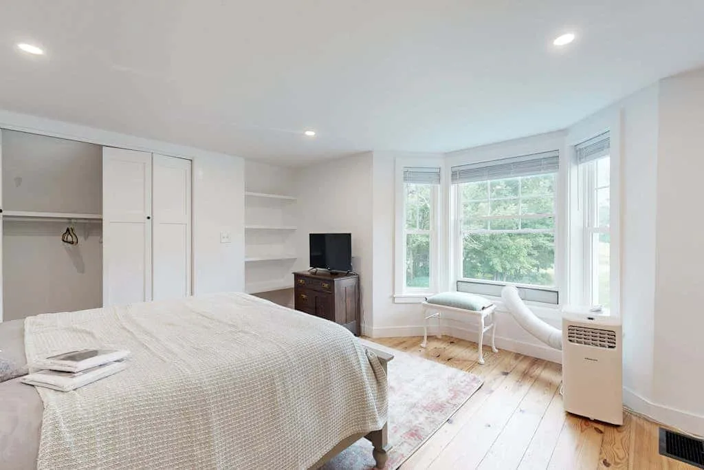 A bright bedroom with a large bed and a sitting area beside the windows.
