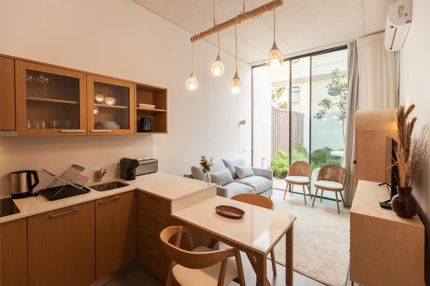 A bright studio interior combines a kitchen, dining table, and seating area beside glass doors.