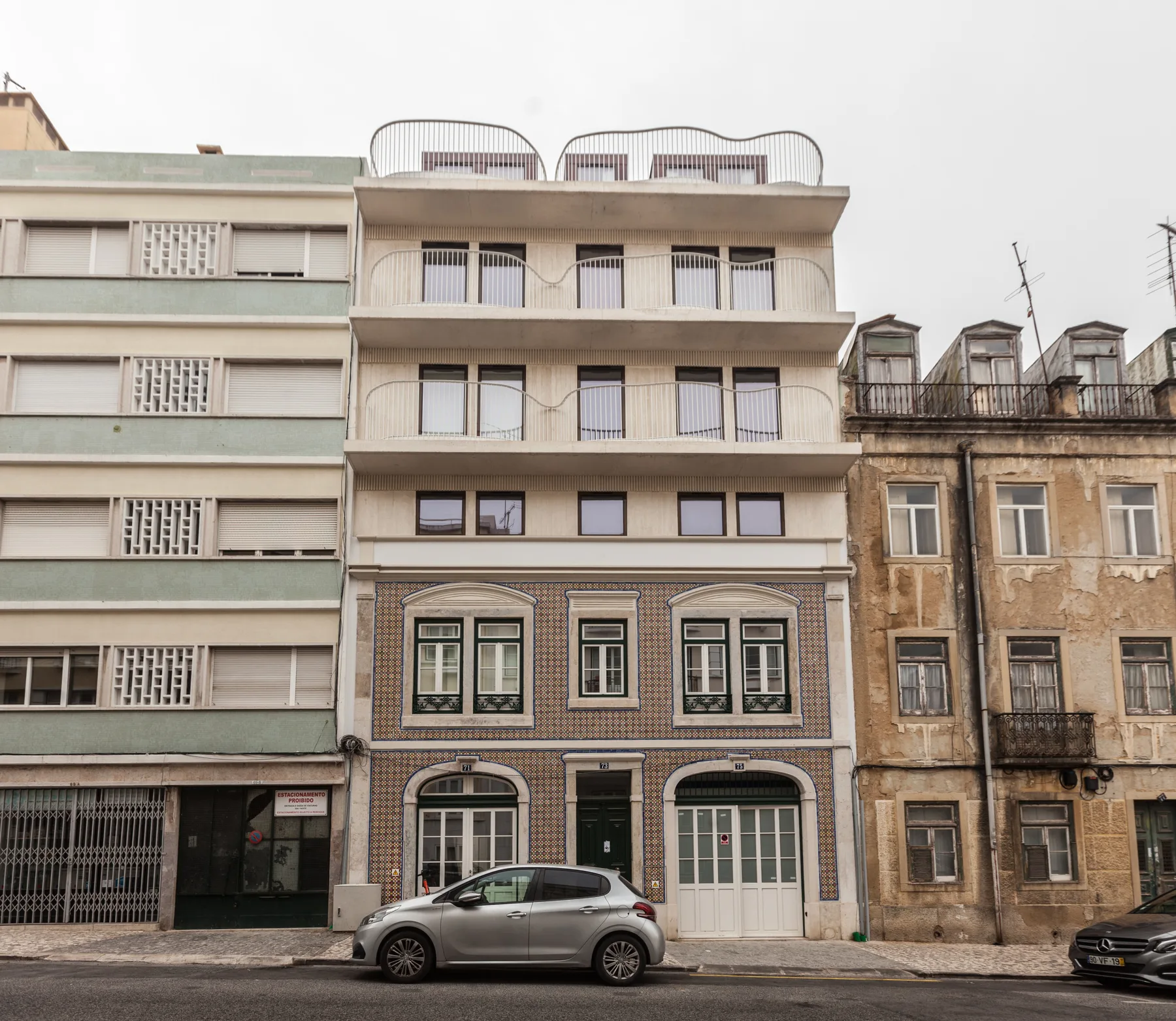 Vista de una calle con un edificio estrecho de varias plantas entre dos fachadas vecinas.