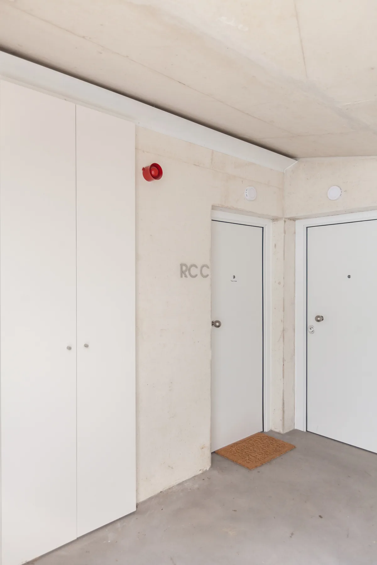 Un pasillo interior con dos puertas y un armario blanco alto.