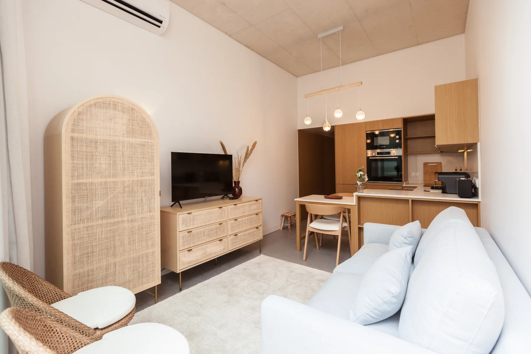 A bright studio living area with seating, a television, and an open kitchen.