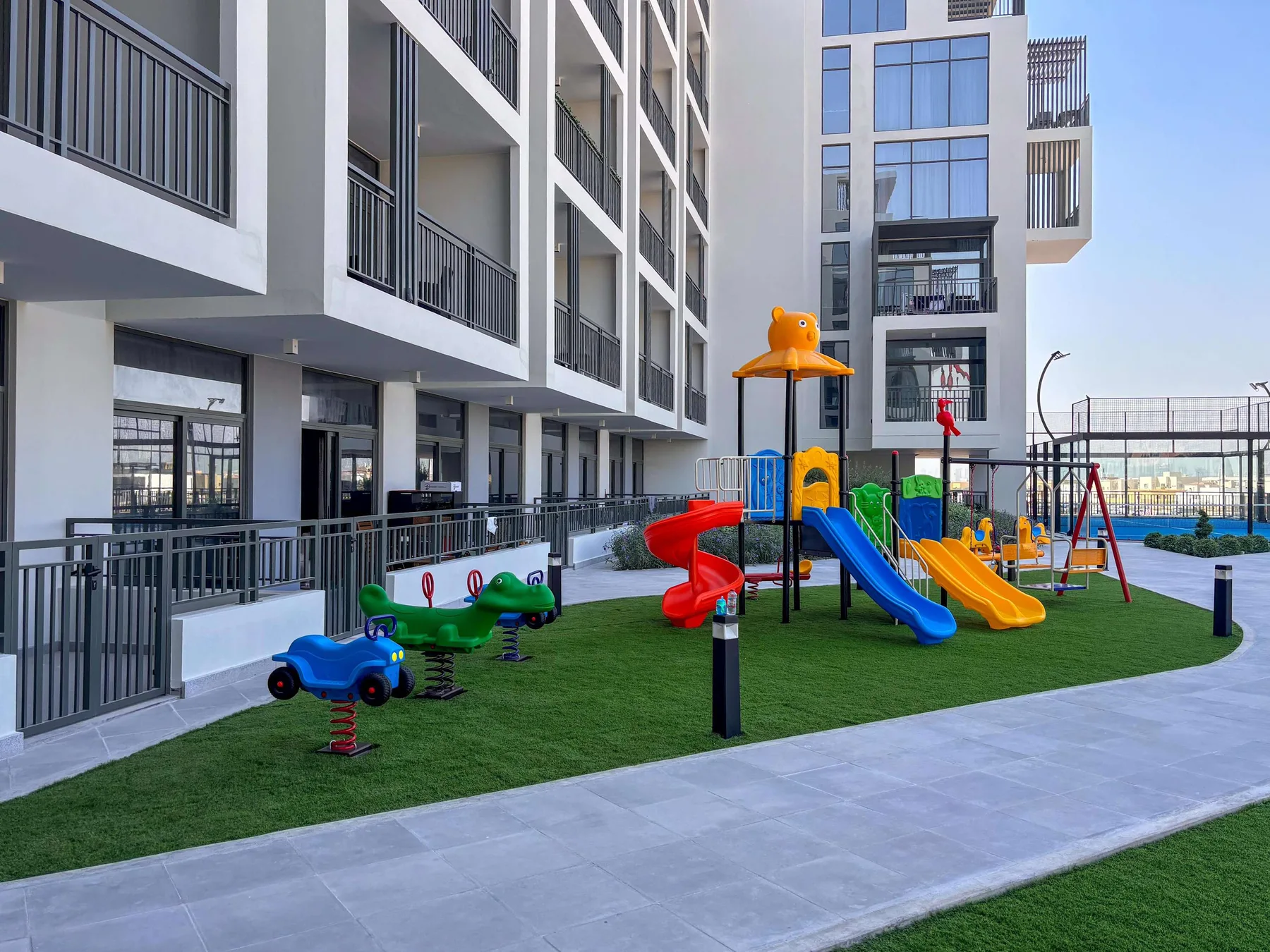 Un parque infantil con toboganes y juegos de colores está junto a un edificio de apartamentos moderno.