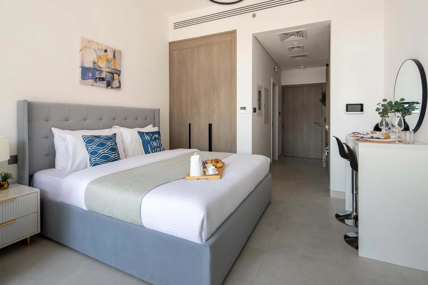 Un dormitorio con una cama grande, cabecero gris tapizado y una pequeña zona de escritorio.