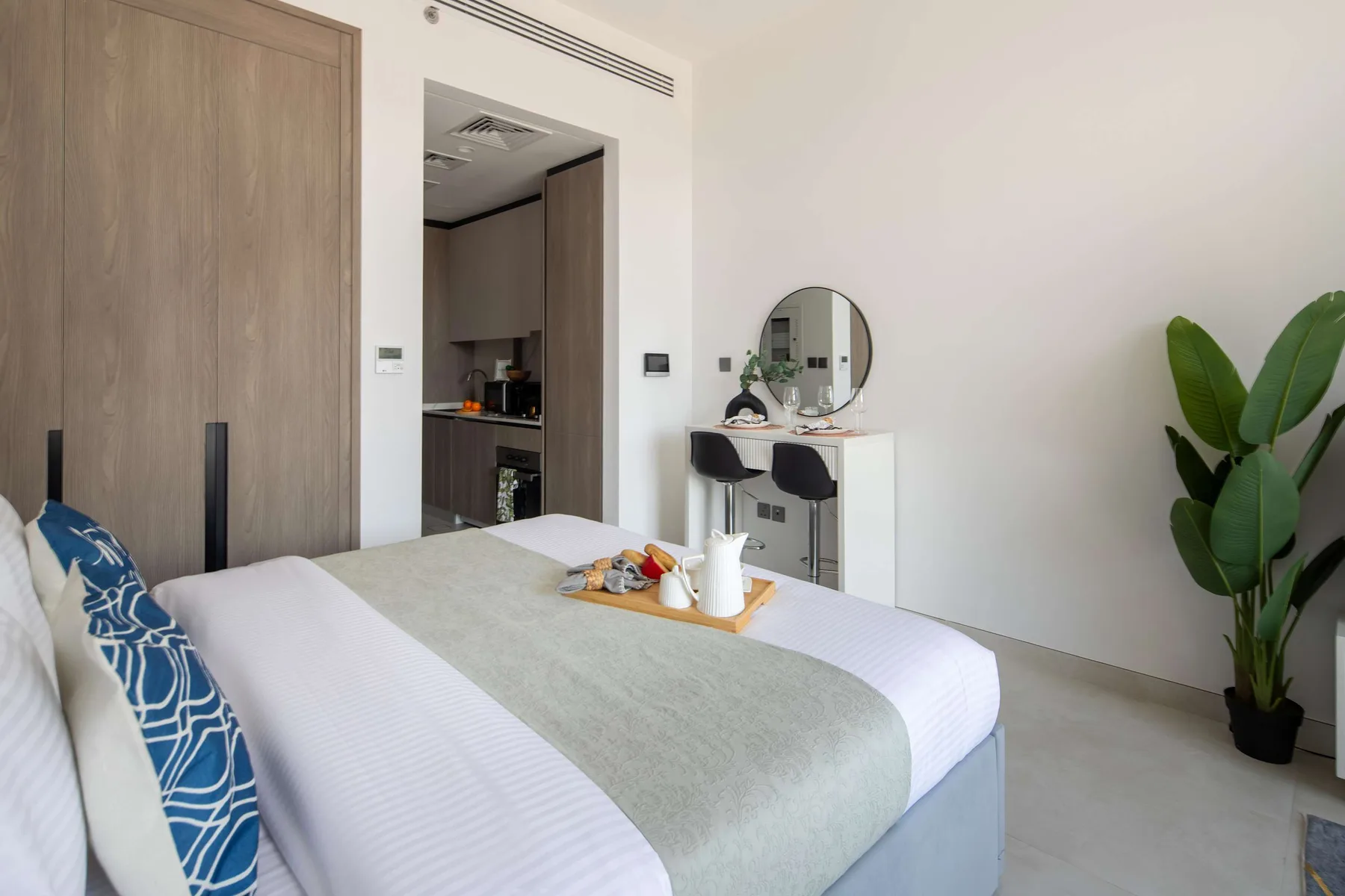 Un dormitorio con una cama bien tendida, un tocador y una planta en maceta.