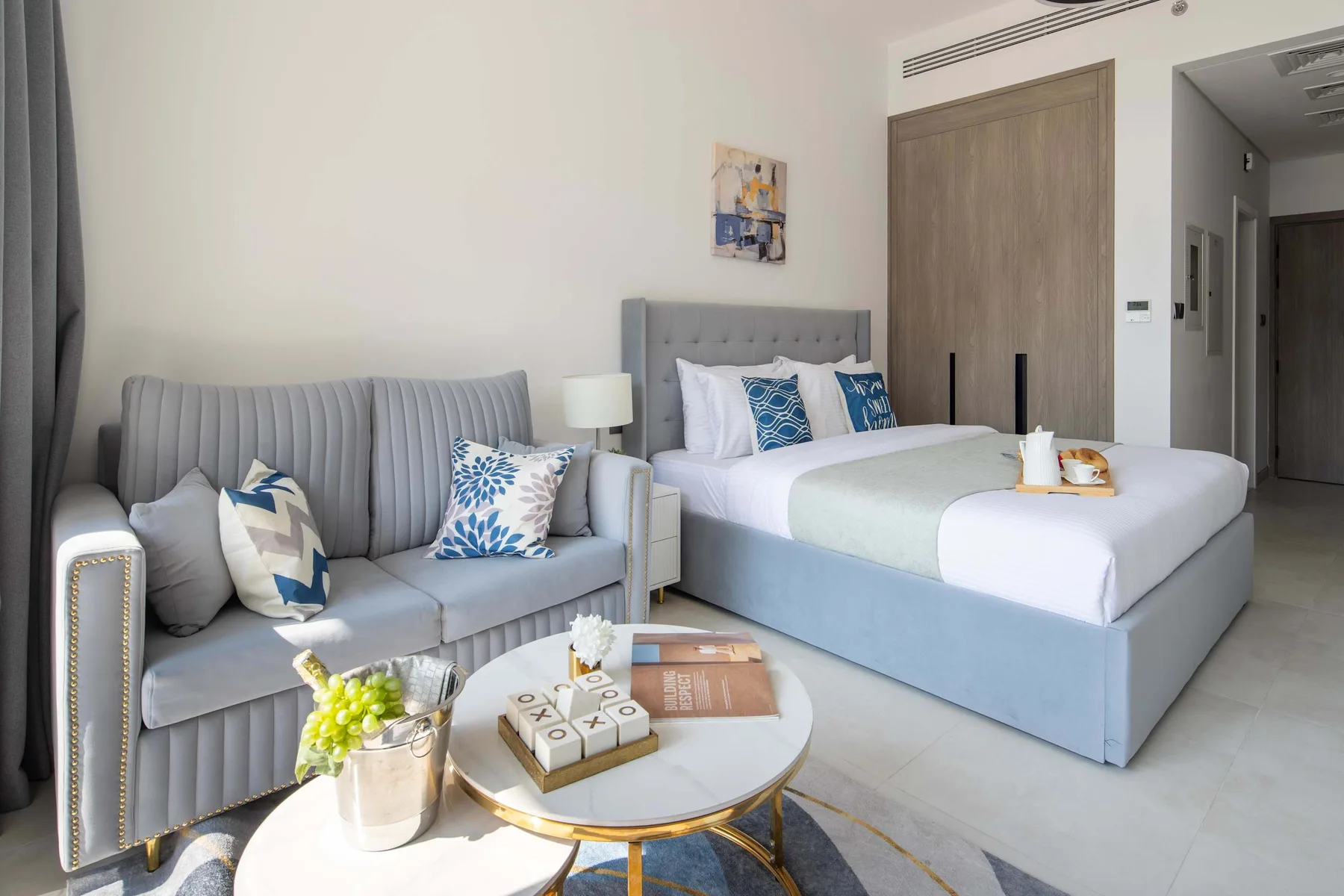 Un dormitorio con una cama y asientos grises junto a una mesa de centro redonda.