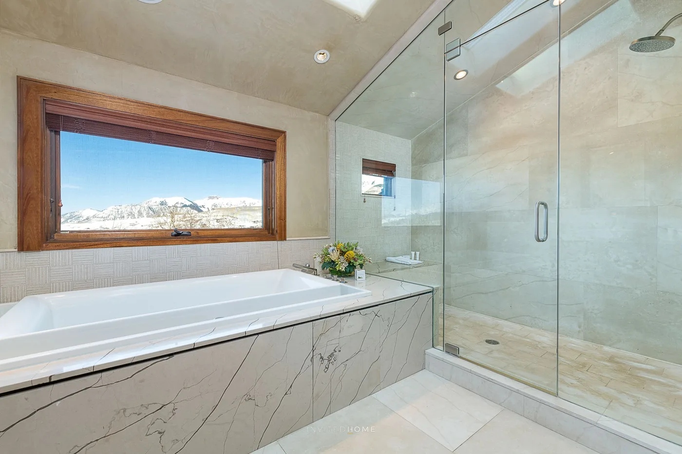 Un baño luminoso tiene una bañera junto a una ducha de cristal y una ventana amplia.