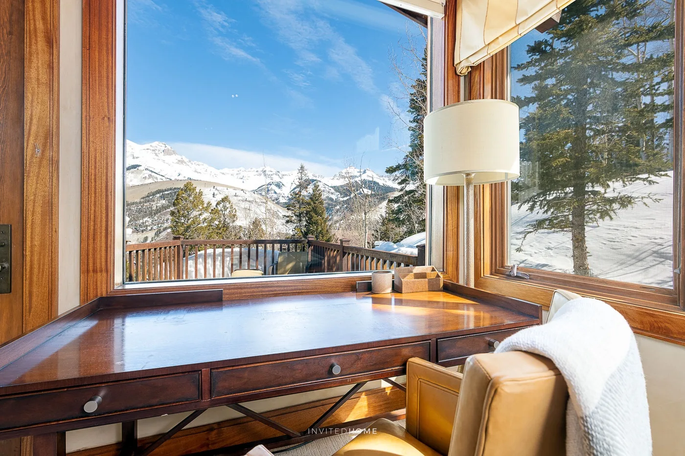 Un escritorio de madera junto a grandes ventanales ofrece vistas de montañas nevadas.