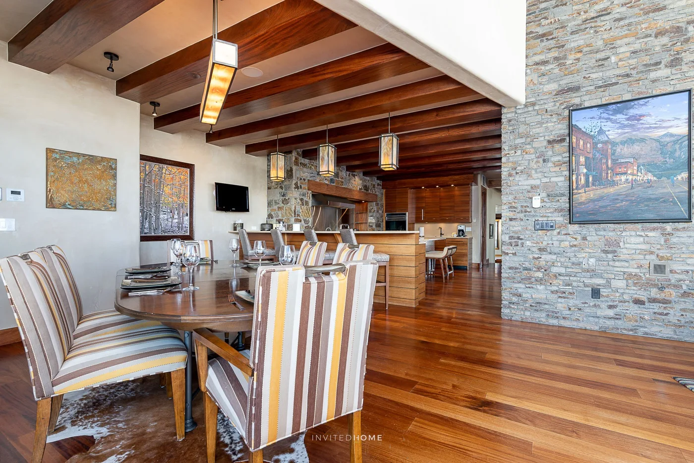 Un comedor abierto con asientos a rayas y una mesa de madera bajo vigas expuestas.