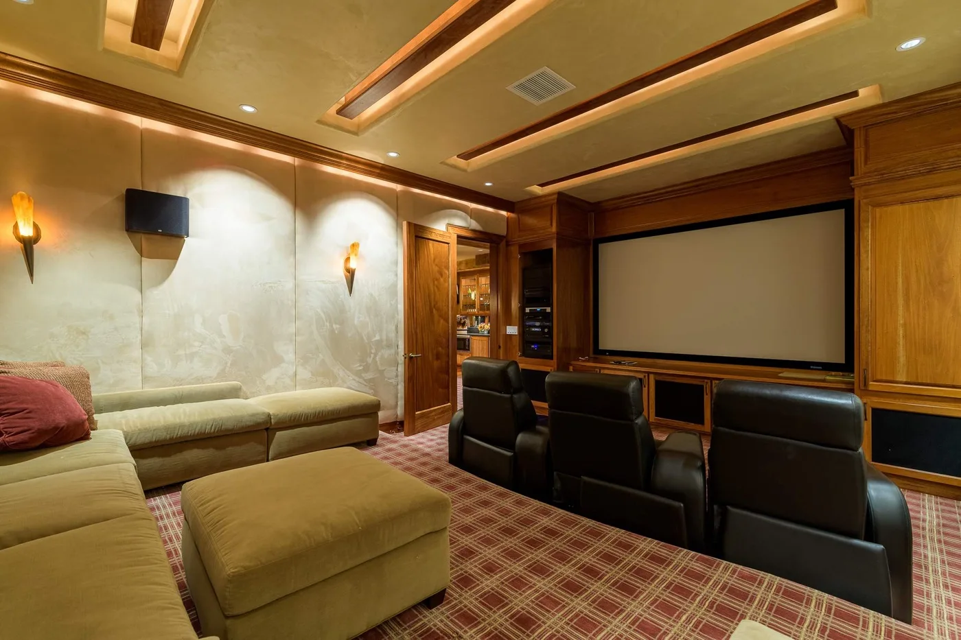 Una sala de cine en casa tiene una pantalla grande, asientos en filas y un sofá seccional.