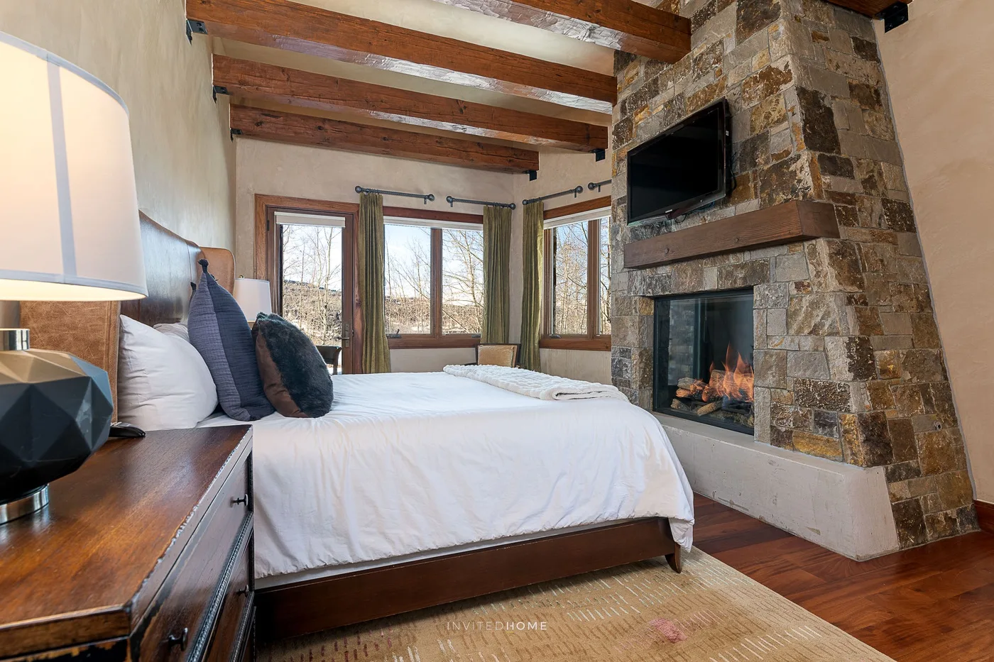 Un dormitorio con una cama, grandes ventanas y una chimenea de piedra.