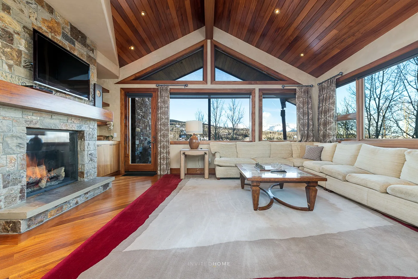 Una sala de estar con chimenea de piedra, asientos claros y grandes ventanas.