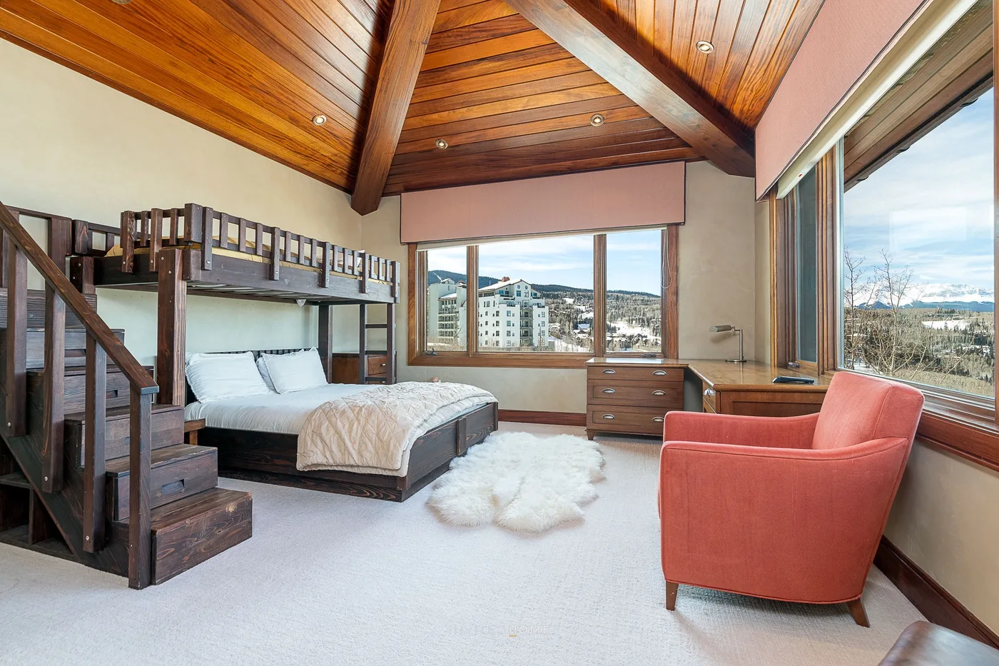 Un dormitorio con una cama tipo loft, un sillón rojo y grandes ventanas.