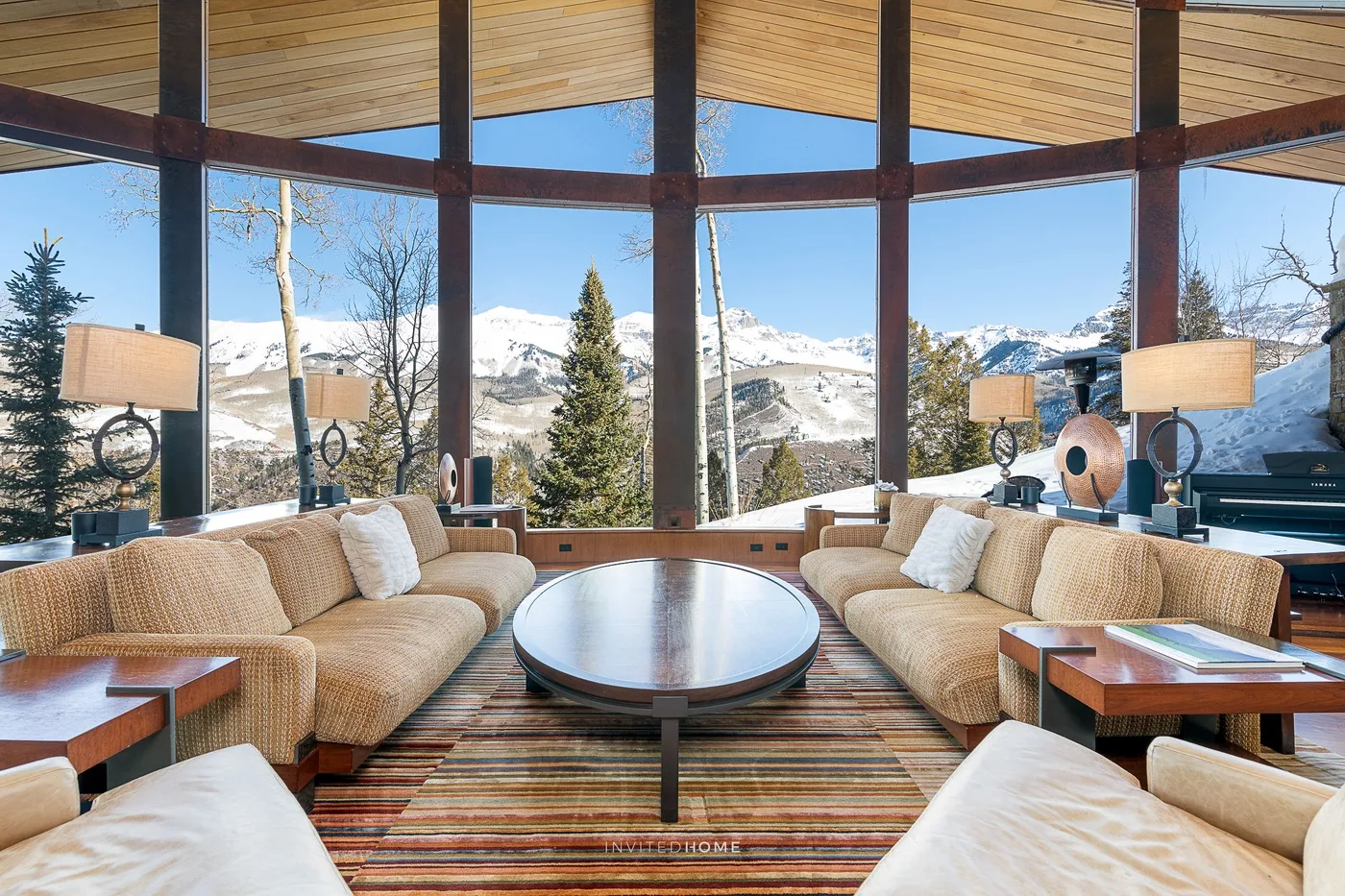 A living room with seating around a low table and large windows overlooking snowy mountains.