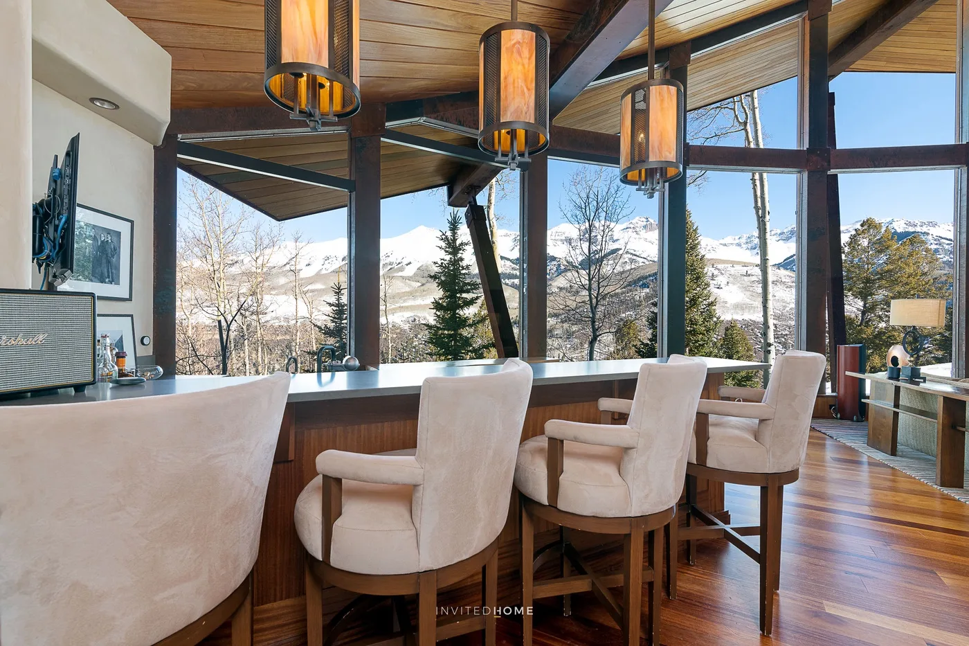 Un comedor con asientos tapizados junto a grandes ventanales con vistas a un paisaje montañoso nevado.