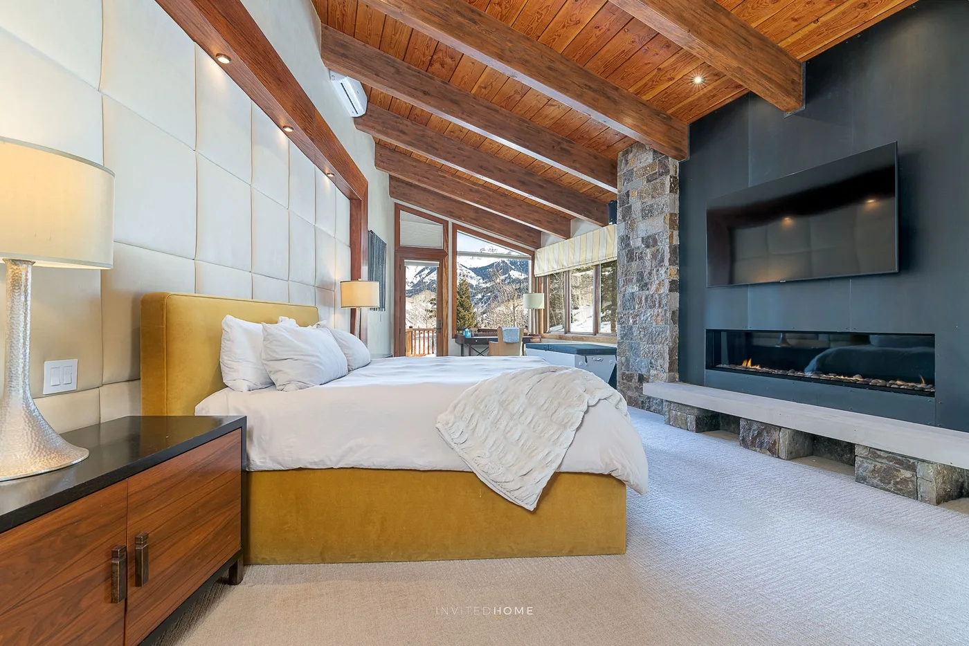 Dormitorio con una cama, techo con vigas de madera y ventanas con vistas a las montañas.