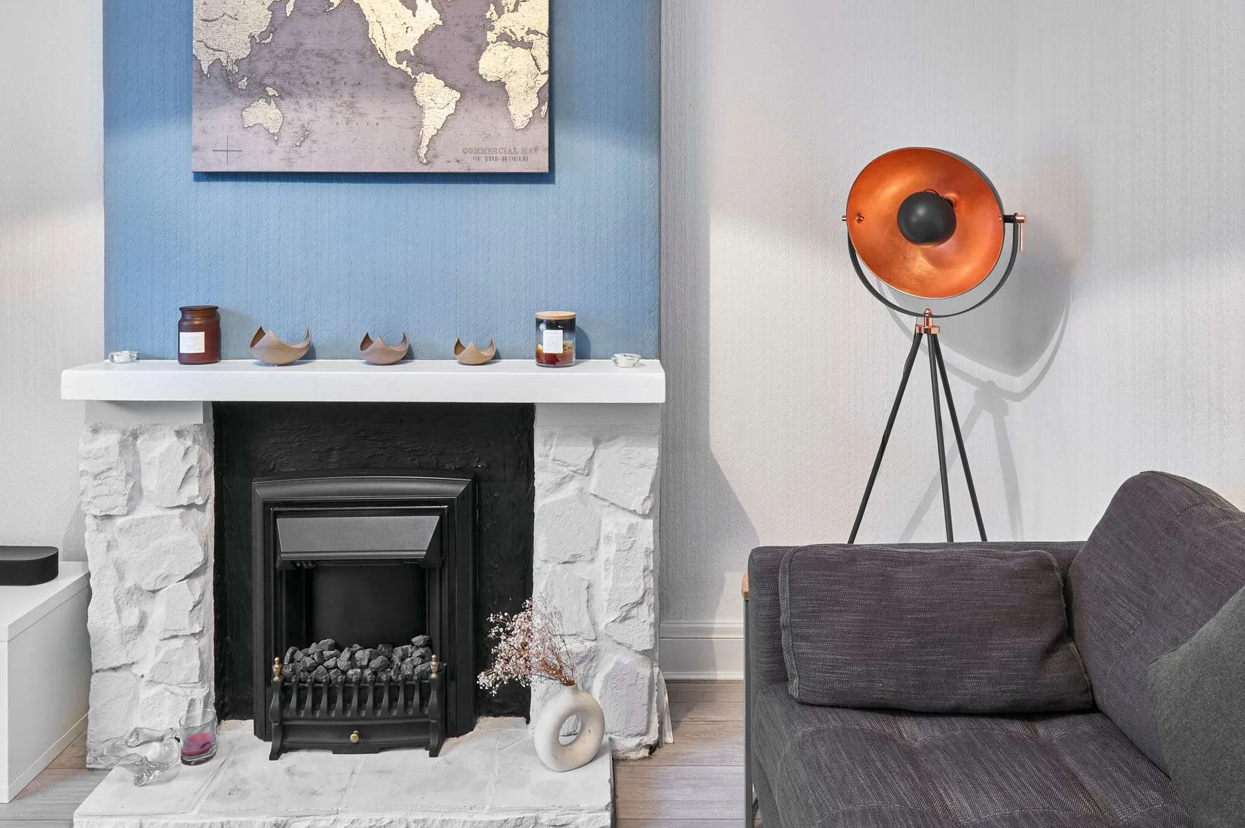 Una sala de estar con chimenea, un sofá gris y una lámpara de pie con trípode.