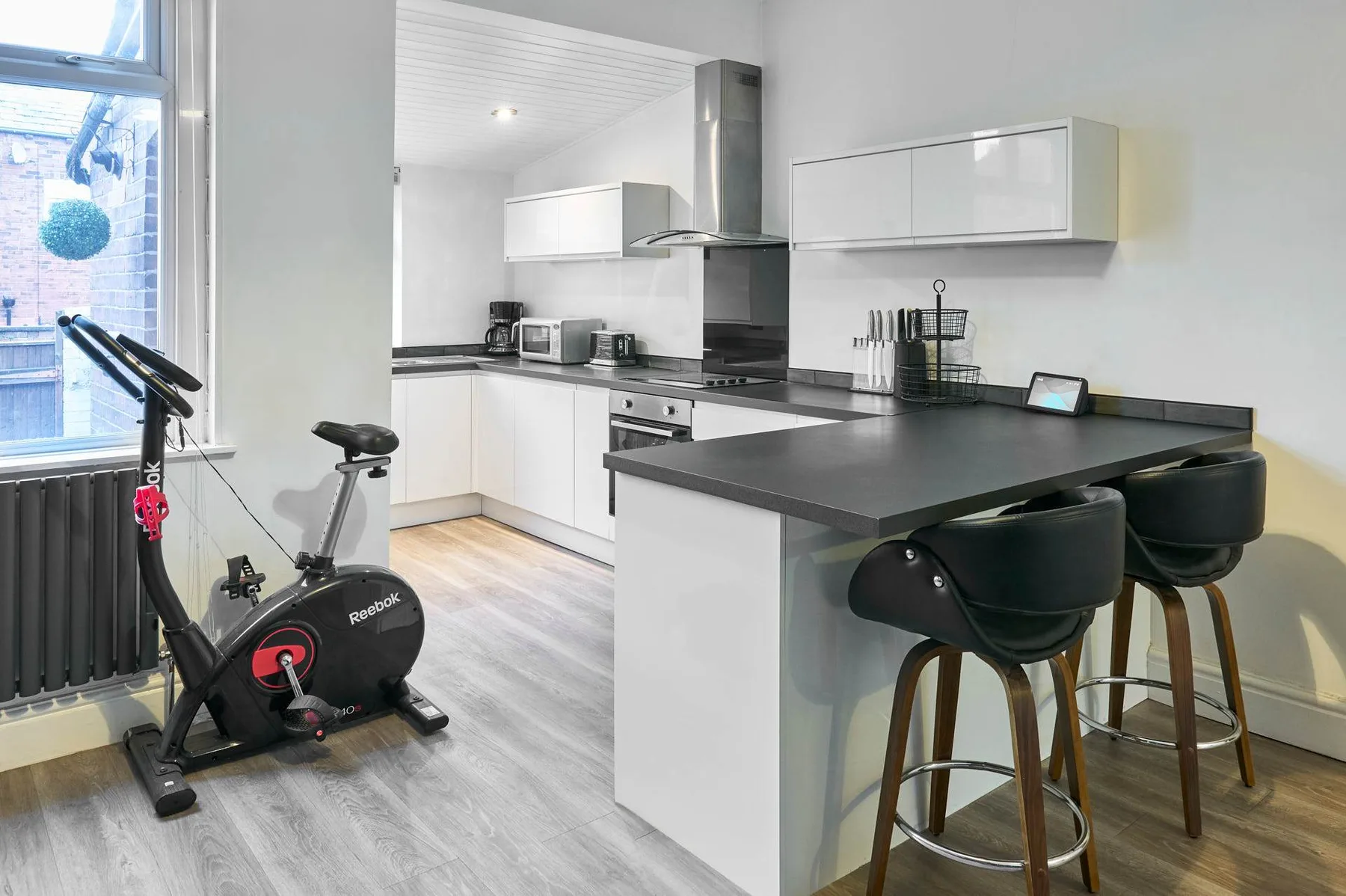 Una cocina moderna con una isla oscura y una bicicleta estática junto a la ventana.