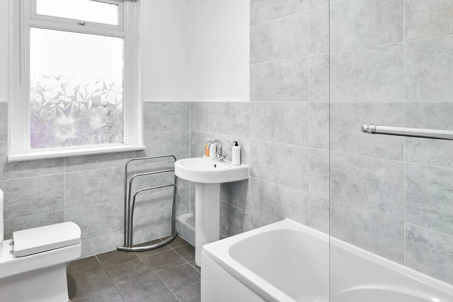 Un baño alicatado con bañera, lavabo con pedestal y ventana translúcida.