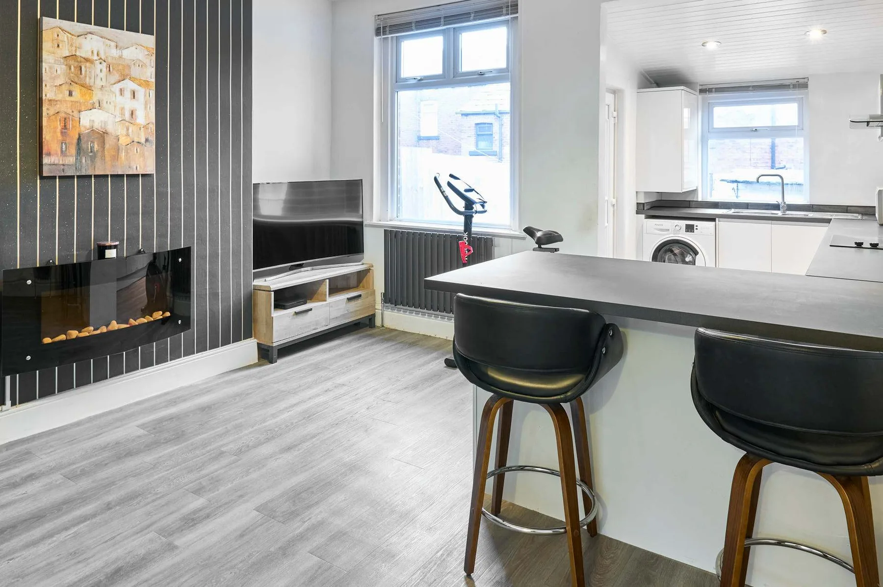 Una sala de estar moderna y abierta tiene una barra de cocina, asientos y una chimenea en la pared.