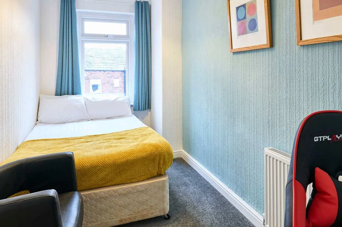 Un dormitorio compacto con una cama bajo una ventana y cuadros enmarcados en la pared.