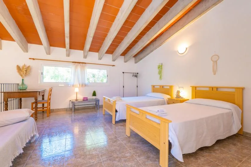 A bright bedroom with wooden beds, a small table, and exposed ceiling beams.
