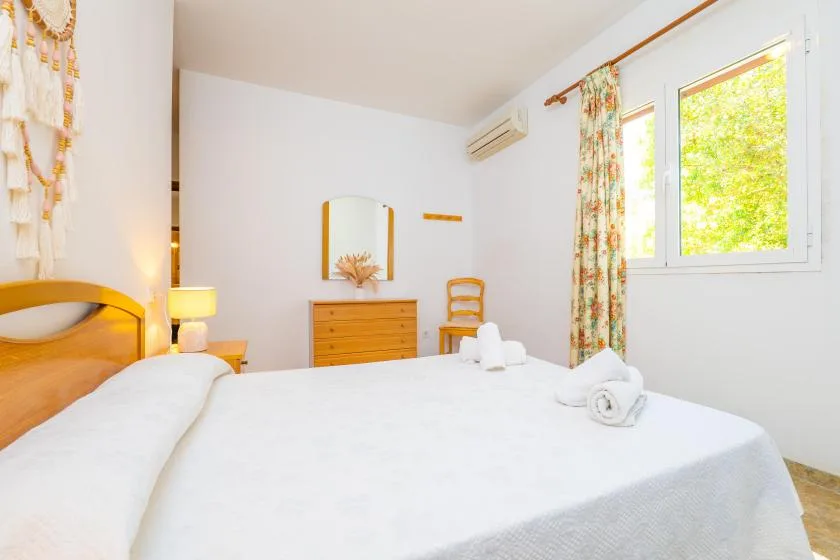 A bright bedroom with a made bed, dresser, and window.