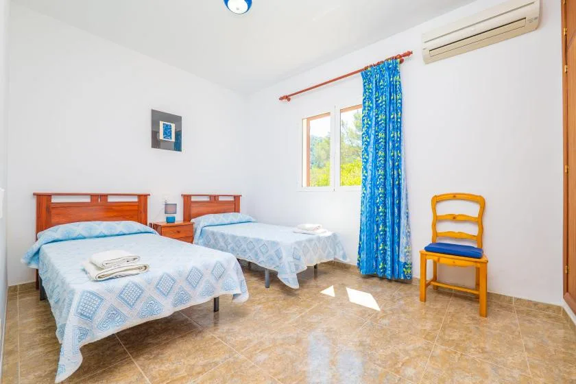 A bright bedroom with two beds, a window, and a blue curtain.