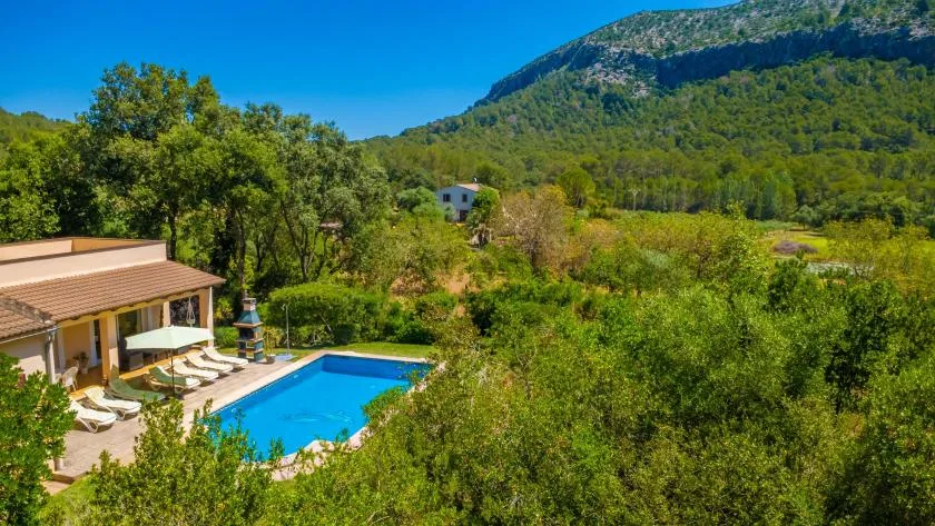 A swimming pool and nearby house sit among green hills and trees.
