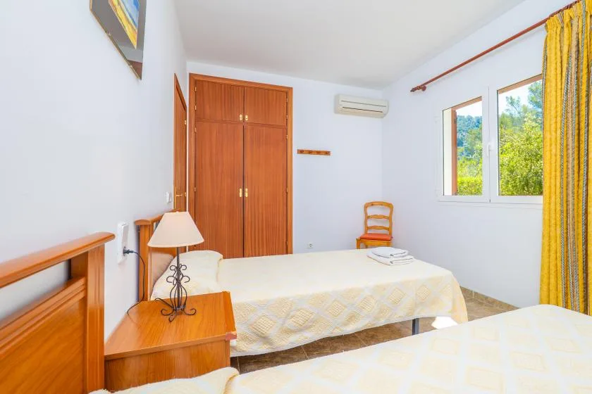 A bedroom with two beds, wooden wardrobes, and a window overlooking greenery.