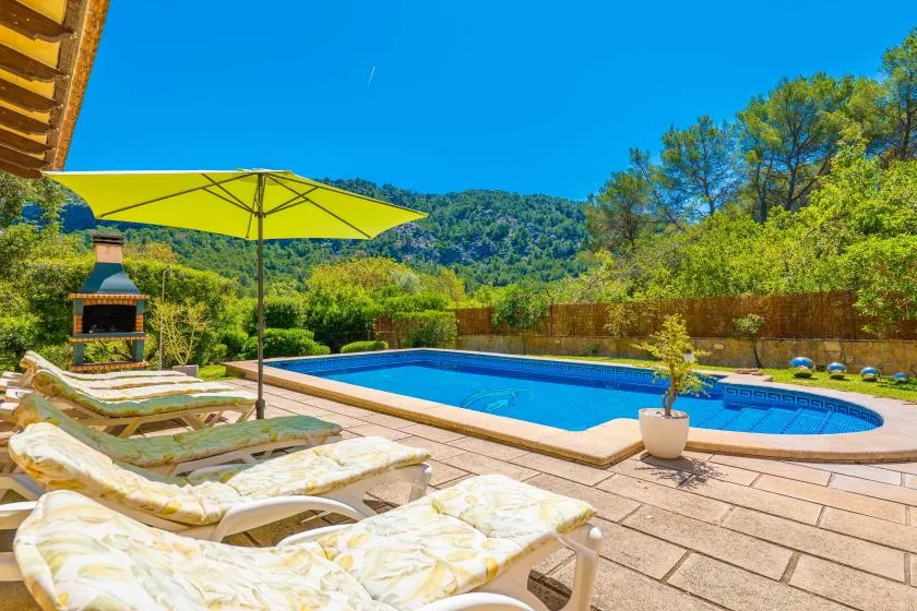 An outdoor swimming pool beside lounge seating, with green hills in the background.