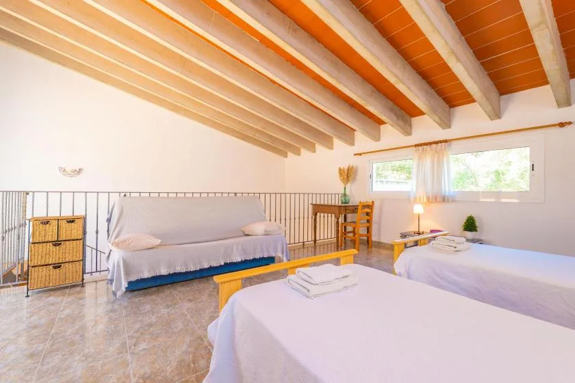 A bright bedroom with beds, a small seating area, and exposed ceiling beams.