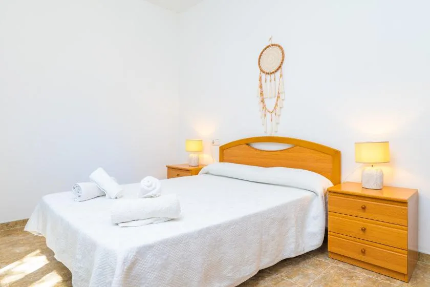 A bright bedroom with a bed, bedside tables, and a hanging wall decoration.