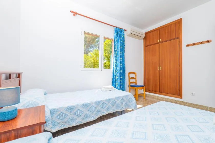 A bright bedroom with two beds, a wooden wardrobe, and a blue curtain.