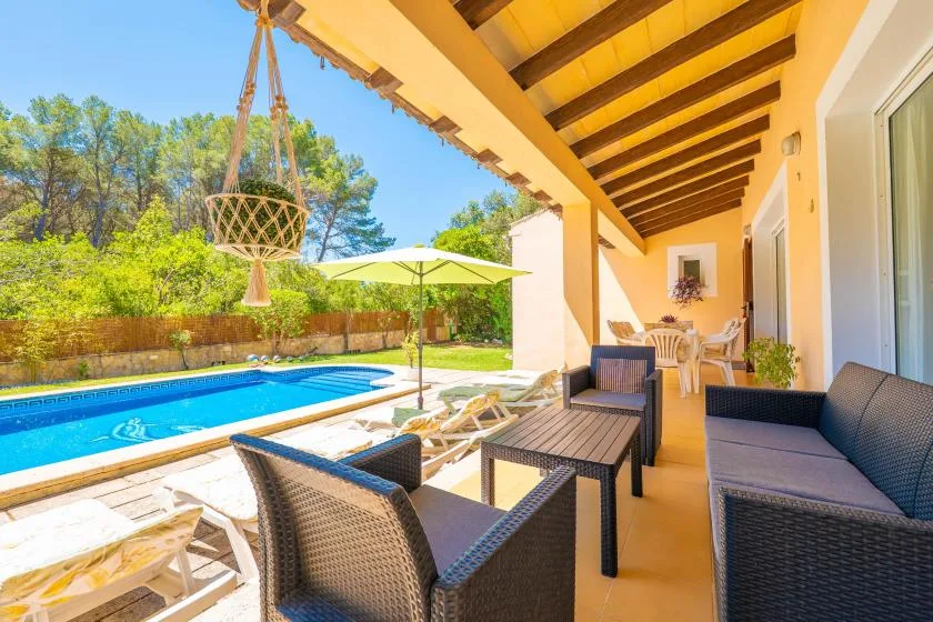 A covered outdoor patio overlooks a swimming pool, with seating and a dining table.