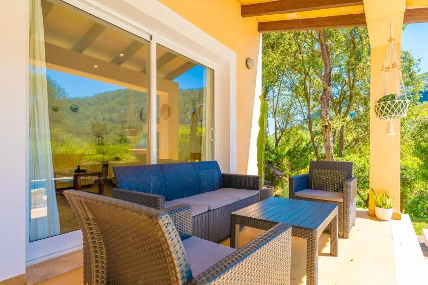 A sunny patio with outdoor seating beside large glass doors and a leafy garden.