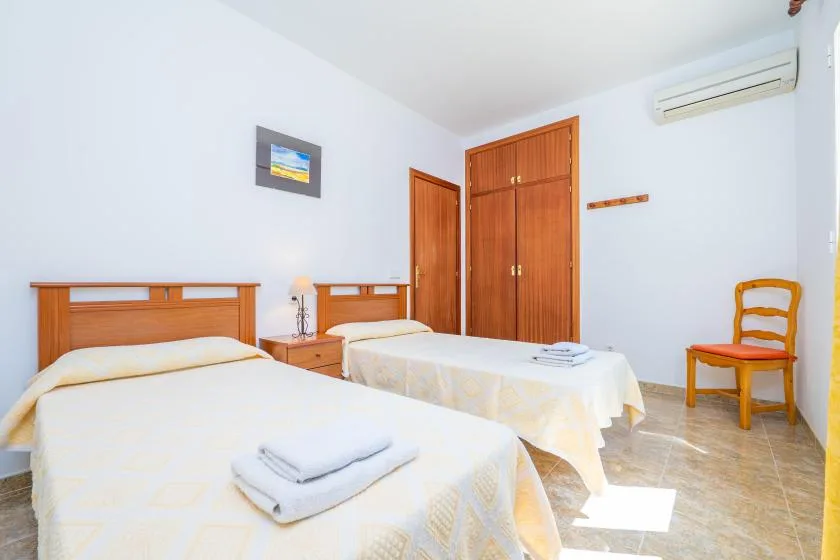 A bright bedroom with two beds, a wooden wardrobe, and a chair.