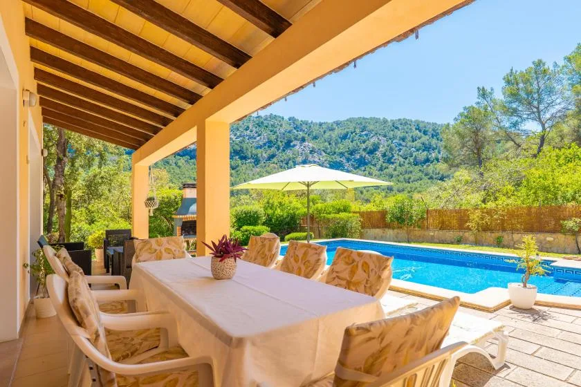 A covered outdoor dining area overlooks a swimming pool and green hills.