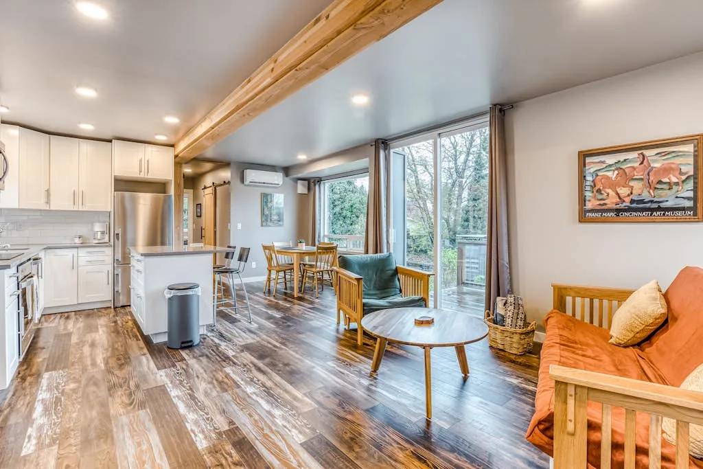Sala de estar y cocina de concepto abierto, con mesa de comedor y asientos junto a grandes ventanas.