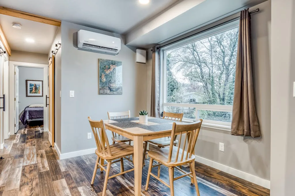 Comedor con una mesa de madera y sillas junto a una ventana grande.