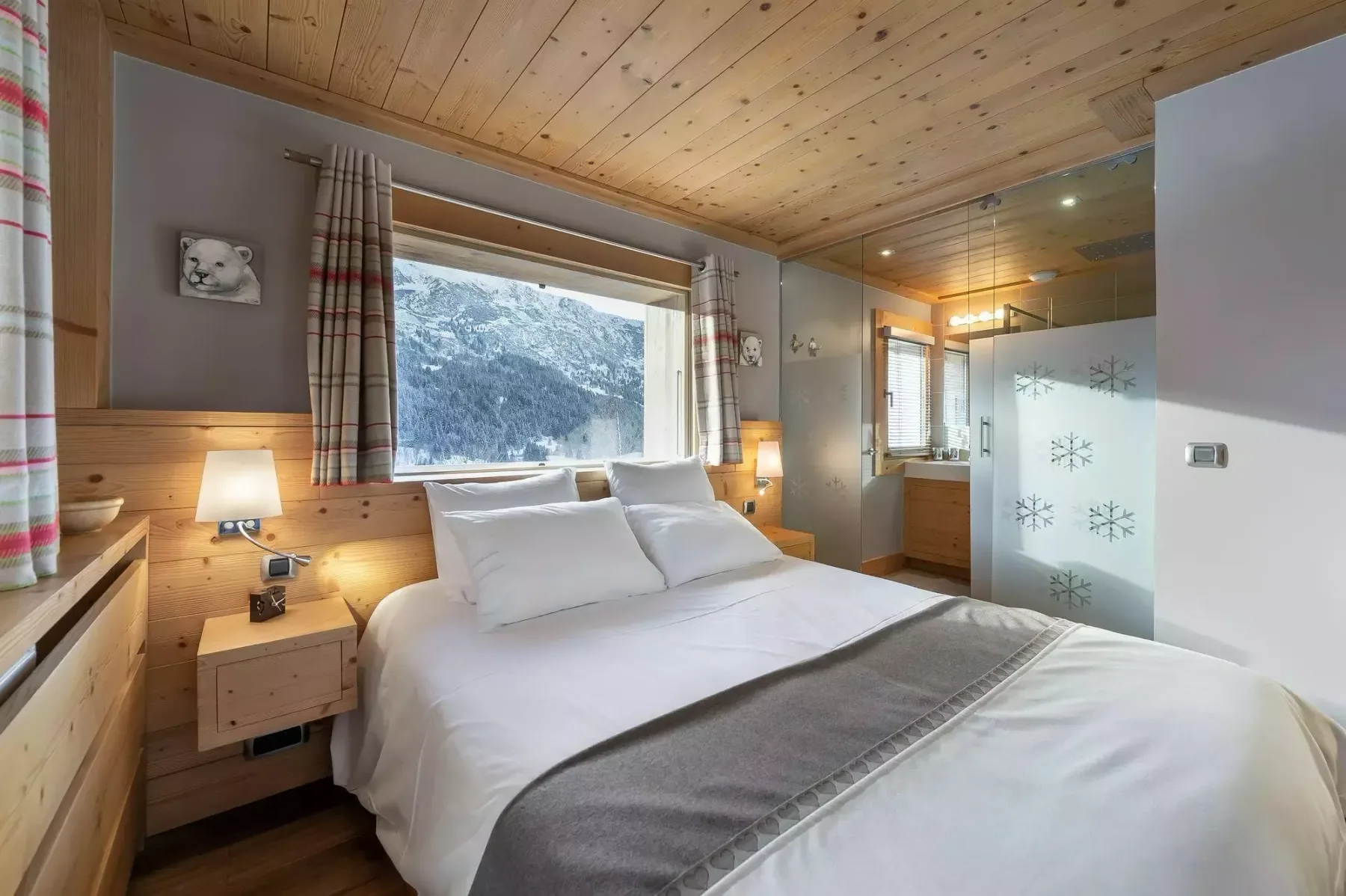 Un dormitorio con una cama bien hecha y una gran ventana con vistas a montañas nevadas.