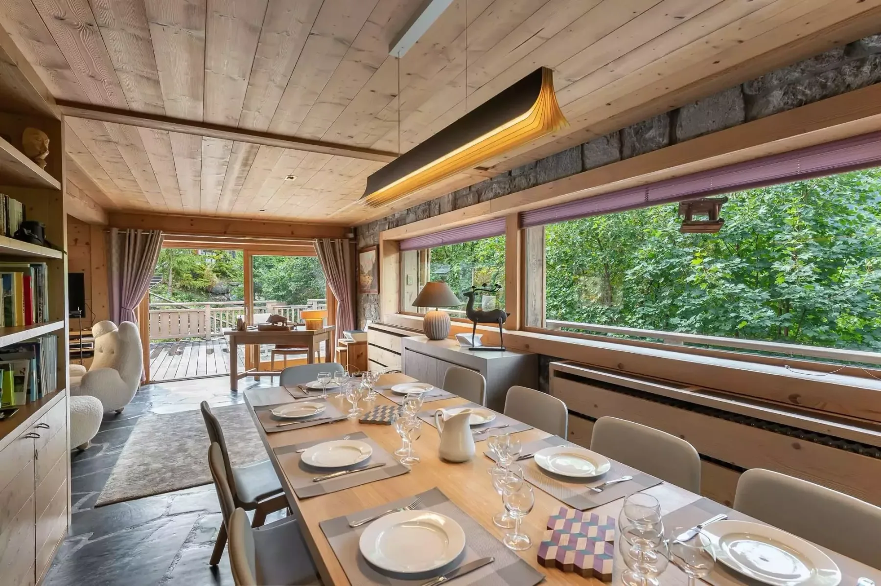 Comedor con la mesa puesta junto a grandes ventanales con vistas a la vegetación.