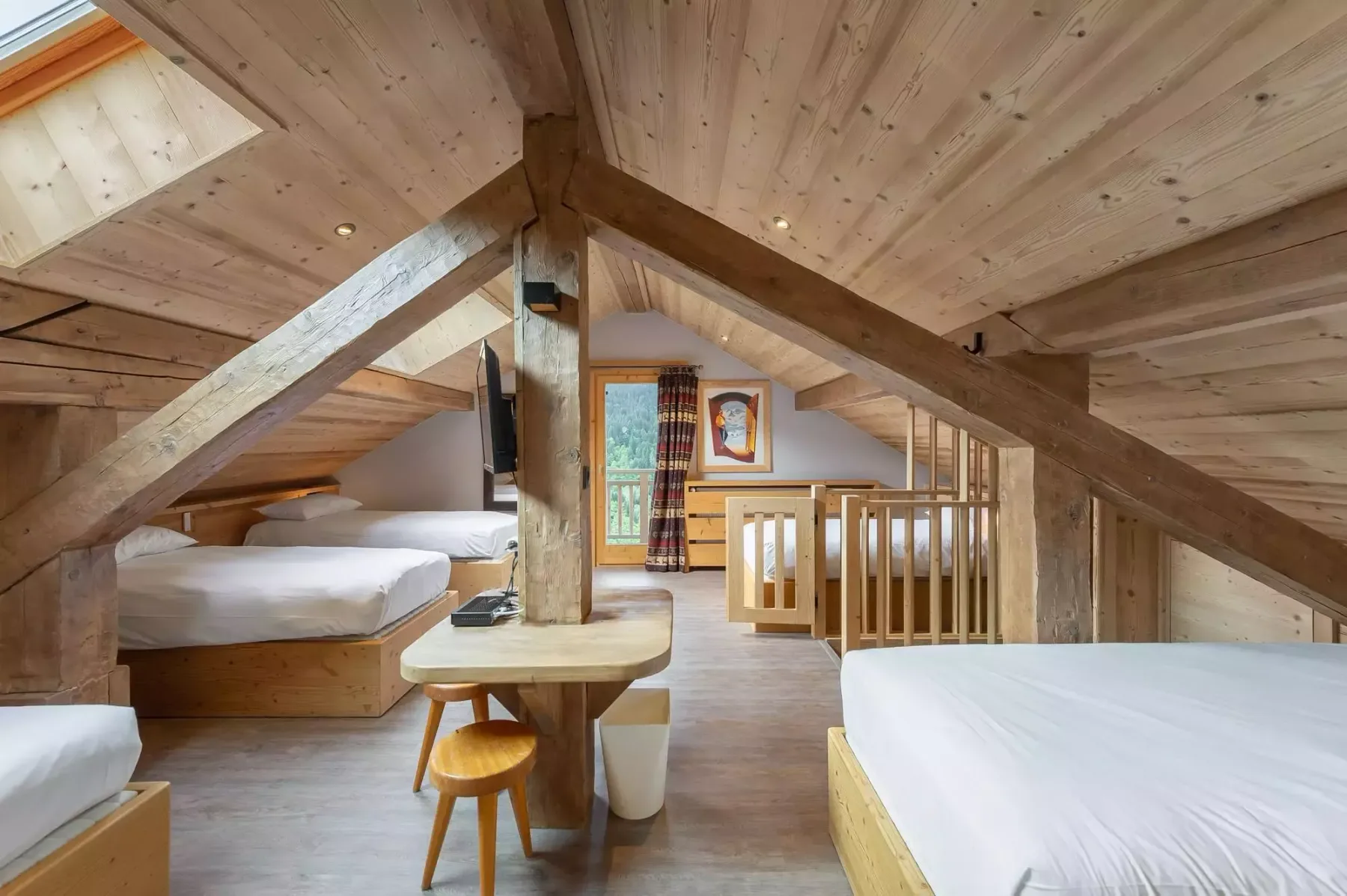 Dormitorio tipo loft con vigas de madera, camas, una mesa pequeña y una barandilla de madera.